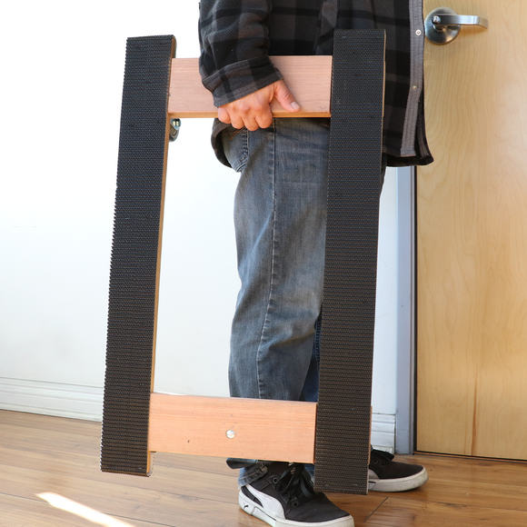 A person is using a solid wood furniture moving dolly with black rubber tread on the caster wheels for anti-slip protection. The dolly has a pre-assembled platform and is designed for easy transportation of furniture.